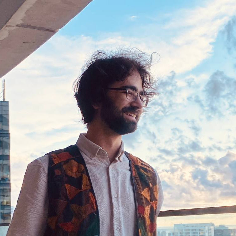 Man wearing a patterned vest standing by a window with a cityscape view